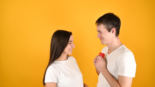 Un homme donne un cœur à une femme sur jaune