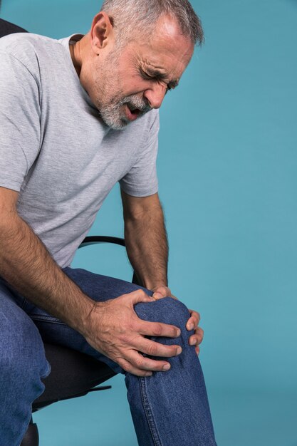 Homme avec douleur au genou assis sur une chaise