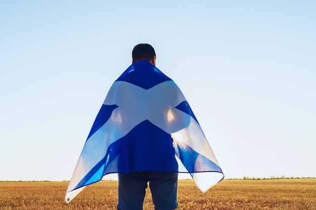 Homme avec un drapeau de l'Écosse debout dans le champ du matin