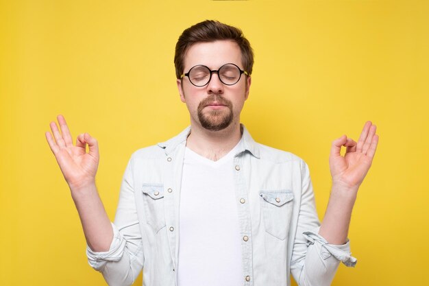 Homme drôle caucasien méditant Studio tourné sur un mur jaune