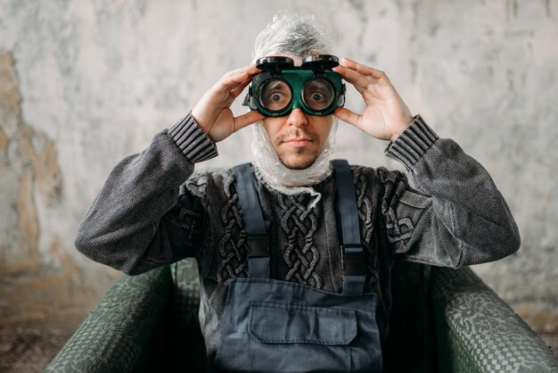 Homme drôle de monstre dans des lunettes de natation assis sur une chaise, intérieur de la salle grunge.