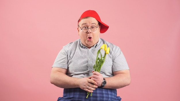 Homme drôle qui ressemble beaucoup à Winnie-the-Pooh avec des tulipes jaunes dans ses mains sur un fond rose isolé