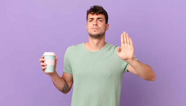 Homme avec du café à l'air sérieux, sévère, mécontent et en colère montrant la paume ouverte faisant un geste d'arrêt