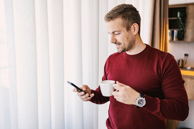 Un homme du matin boit son café et vérifie les messages en ligne sur le téléphone w