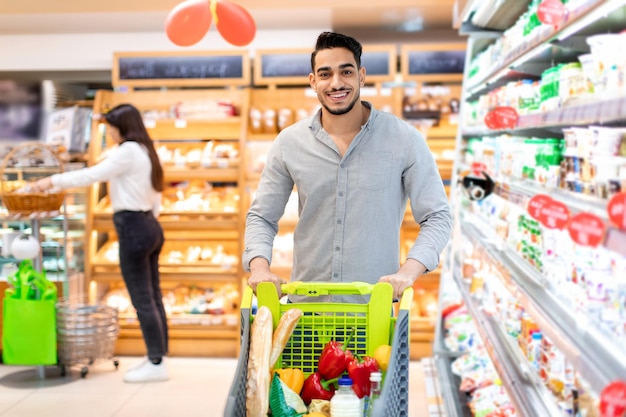 Homme du Moyen-Orient debout avec un chariot de magasin faisant du shopping dans un supermarché