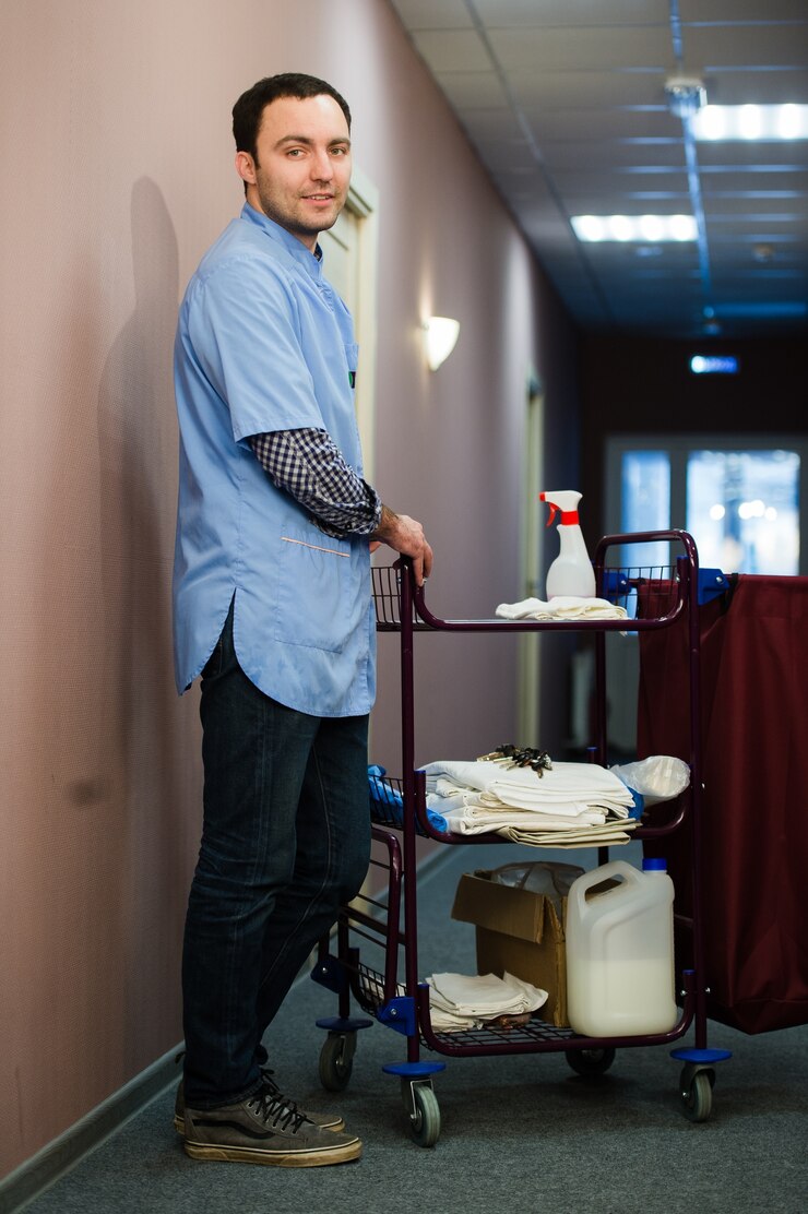 L'homme du personnel de l'équipe de nettoyage de l'hôtel souriant avec un chariot