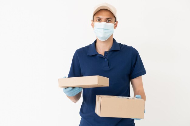 Homme du service de livraison en t-shirt, en masque de protection et gants donnant des commandes de nourriture et tenant des boîtes sur fond blanc.