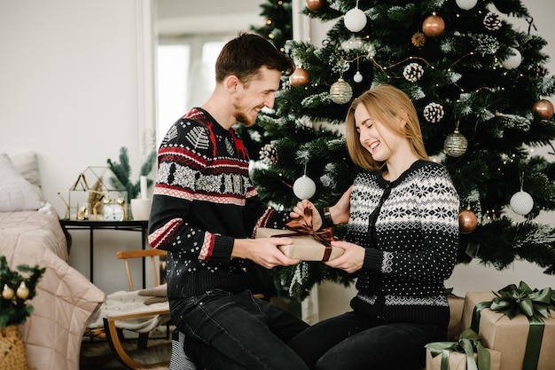 Homme échangeant des cadeaux avec une femme près d'un arbre Jeune couple joyeux avec un cadeau amoureux Couple célébrant Noël ensemble à la maison Joyeux Noël et joyeuses fêtes Bonne année 2021