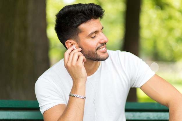 Homme écoutant de la musique assis sur un banc dans un parc par une chaude journée d&#39;été ensoleillée