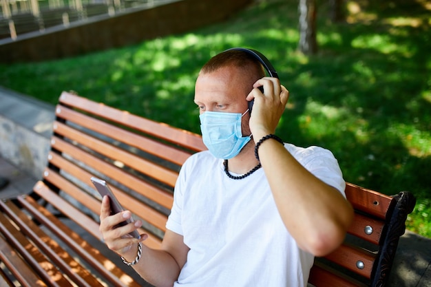 Homme écoutant de la musique avec un casque, à l'aide d'un smartphone portant un masque de protection du visage en plein air dans le parc, mode de vie nouveau normal, quarantaine, coronavirus