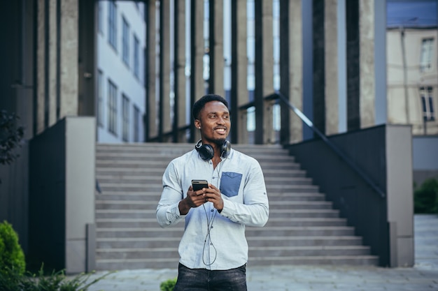 L'homme écoutant de la musique utilise de gros écouteurs, marche dans la rue, heureux afro-américain