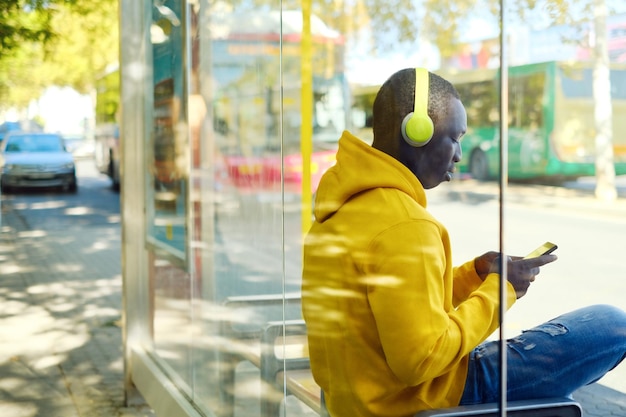 Un homme écoute de la musique assis à l'arrêt de bus.