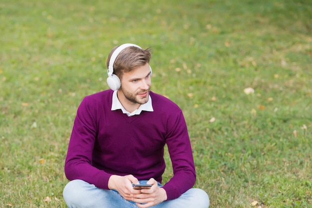 L'homme écoute de la musique dans les écouteurs du smartphone. beau mec dans les écouteurs utilise un téléphone portable. technologie de la vie moderne. lecteur mp3. obtenir des informations à partir d'un livre audio. concept d'apprentissage en ligne.