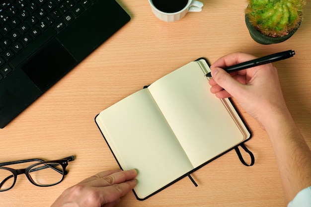 L'homme écrit sur un cahier sur un bureau en bois. Bureau, travail à domicile