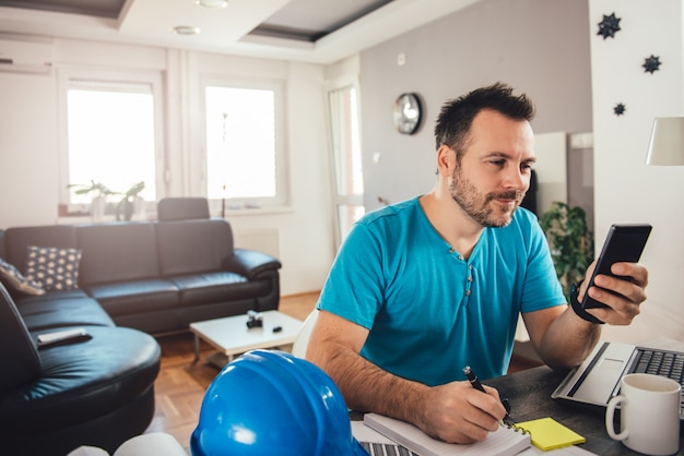 Homme écrivant des notes et tenant un téléphone intelligent