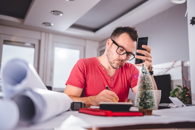 Homme écrivant des notes et tenant un téléphone intelligent