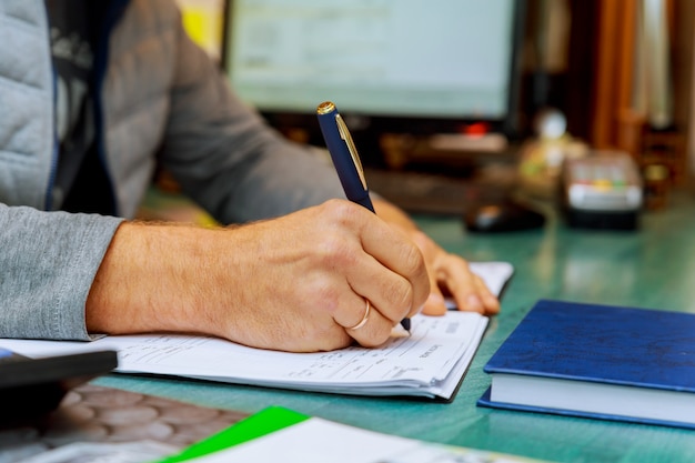 Homme écrivant sur papier avec un stylo sur la table.