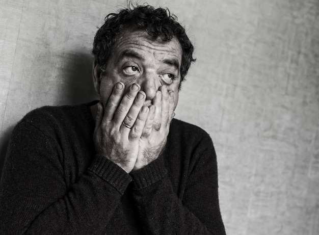 Un homme effrayé couvre sa bouche en détournant le regard vers le mur.