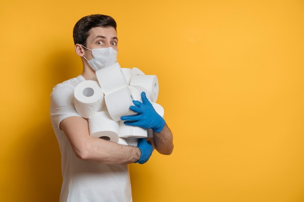 Un homme effrayé dans un masque protecteur contre le virus Covid-19 tient dans ses mains de nombreux rouleaux de papier toilette