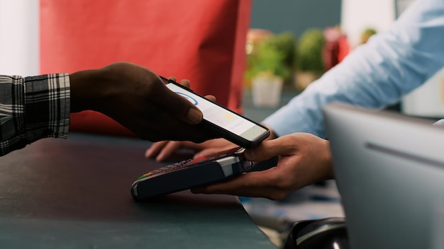 Homme élégant achetant des vêtements à la mode payant avec un téléphone portable au comptoir du magasin de mode. Client afro-américain achetant des vêtements de cérémonie dans une boutique moderne. Notion de mode