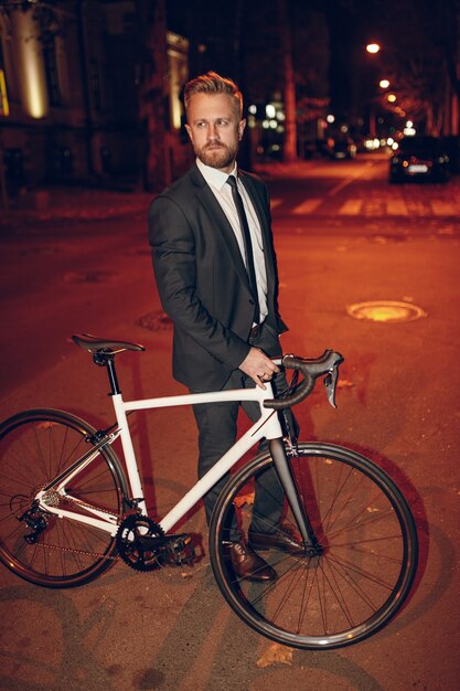 Homme élégant en costume formel avec vélo dans la rue de nuit