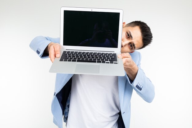 Homme élégant dans une veste bleue montre un écran d'ordinateur portable avec un modèle vierge pour l'insertion d'un site sur un fond de studio blanc.