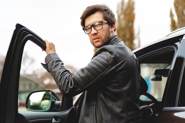 Homme élégant à lunettes est assis dans un portrait de voiture