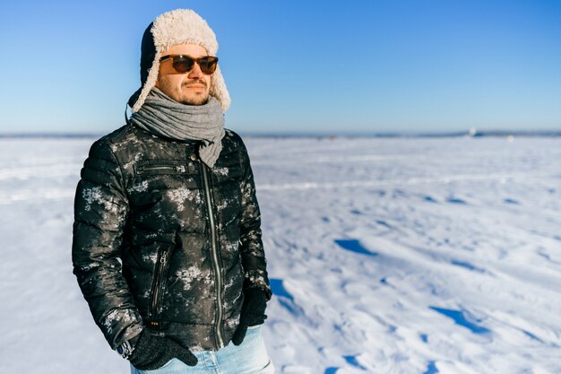 Homme élégant à lunettes de soleil posant dans le champ enneigé