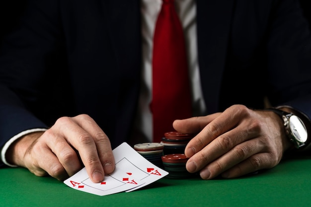 Homme élégant à la table de jeu verte avec des jetons de jeu et des cartes jouant au poker et au blackjack au casino.