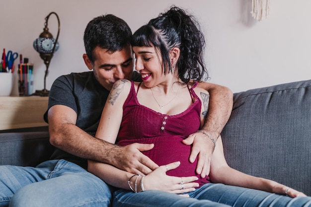 Un homme embrasse et embrasse une femme enceinte alors qu'il est assis sur le canapé à la maison.