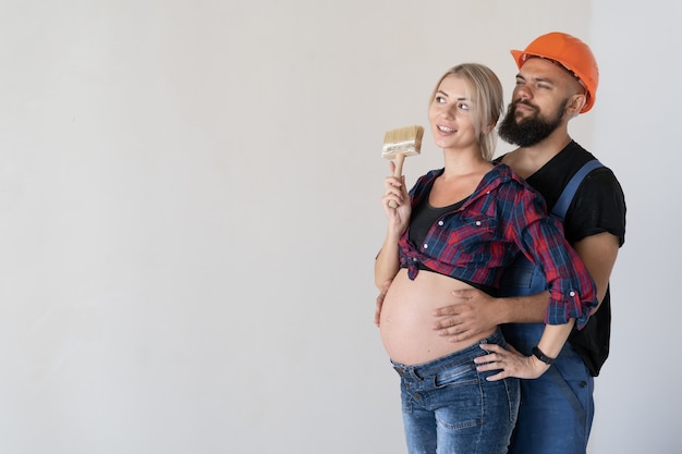 Un homme embrasse sa femme enceinte. uniforme de travail et casque de sécurité orange. la famille heureuse fait la rénovation. Espace de copie.