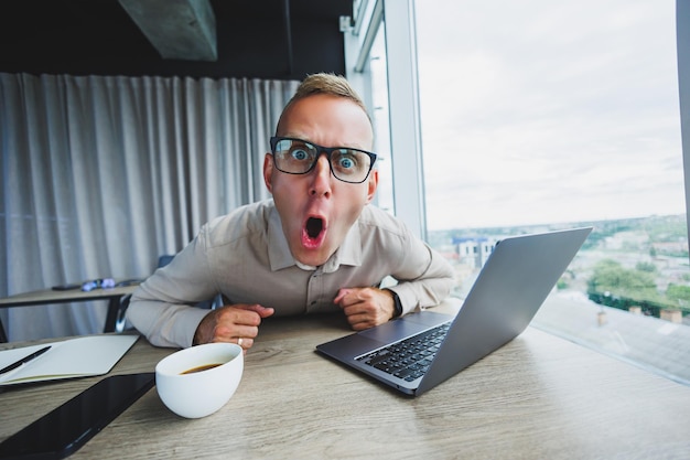 Homme émotif regardant la caméra sur le lieu de travail un homme à lunettes assis devant un bureau avec un ordinateur un étudiant cherche l'inspiration pour de nouvelles idées dans un café de bureau