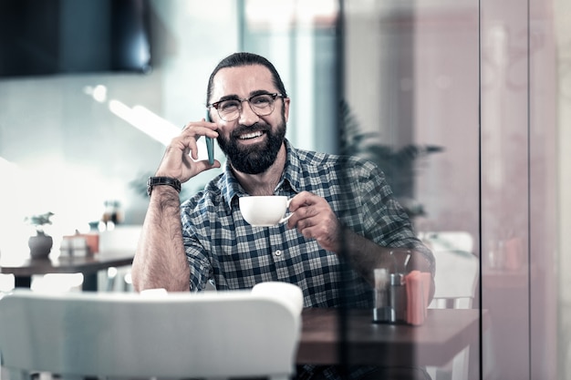 Homme émotionnel. Homme émotionnel barbu se sentir heureux d'appeler son ami de boire du café dans une cafétéria confortable