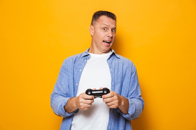 Homme émotionnel isolé sur mur jaune jouer à des jeux avec joystick.