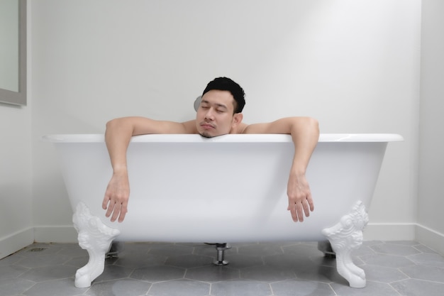 Homme endormi dans une baignoire blanche dans le concept de fatigue et de détente