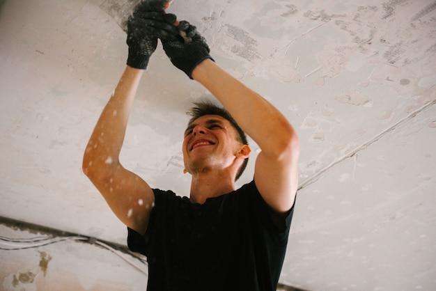 Un homme enlève la vieille peinture du plafond avec une spatule