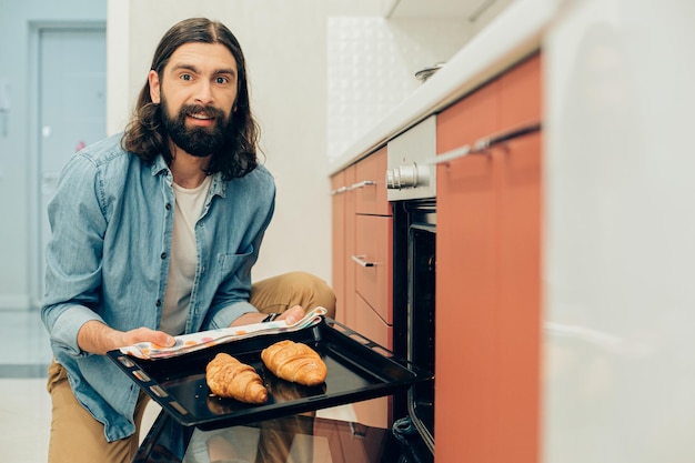 Homme enthousiaste tenant un plat de cuisson avec de délicieux croissants frais dessus