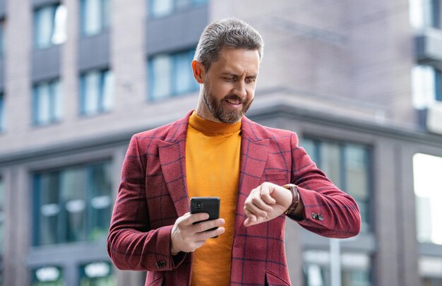 Homme envoyant des messages sur un smartphone vérifier l'heure à l'extérieur photo d'un homme envoyant des messages sur un smartphone en veste homme envoyant des messages sur un smartphone en extérieur