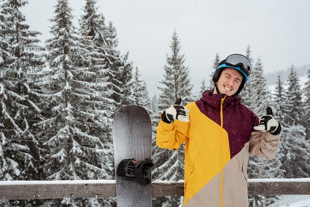 L'homme en équipement de ski, portant des lunettes de sécurité montre les pouces vers le haut, se dresse contre la montagne et les arbres. Sports et loisirs d'hiver, loisirs de plein air.