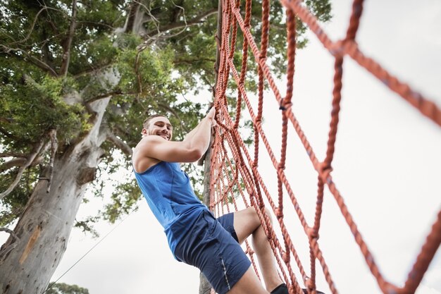 Homme escalade un filet pendant la course d'obstacles dans le camp d'entraînement