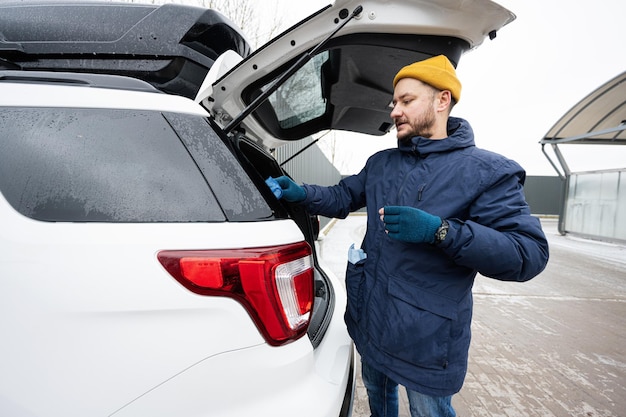 L'homme essuie le coffre d'une voiture SUV américaine avec un chiffon en microfibre après le lavage par temps froid