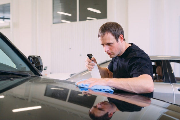 L'homme essuie avec un corps en tissu d'une voiture brillante.