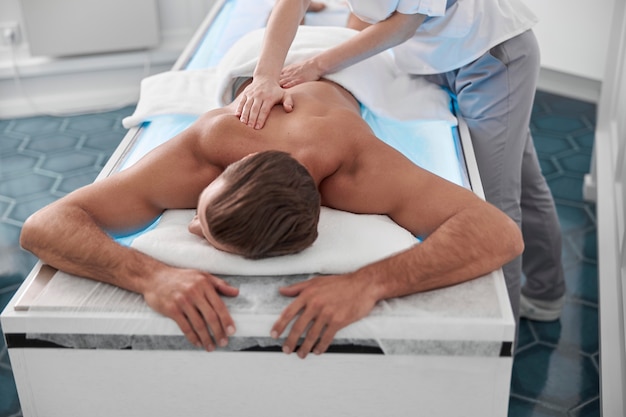 L'homme est allongé sur un canapé confortable pendant que la chiropratique lui fait un massage du dos à l'hôpital