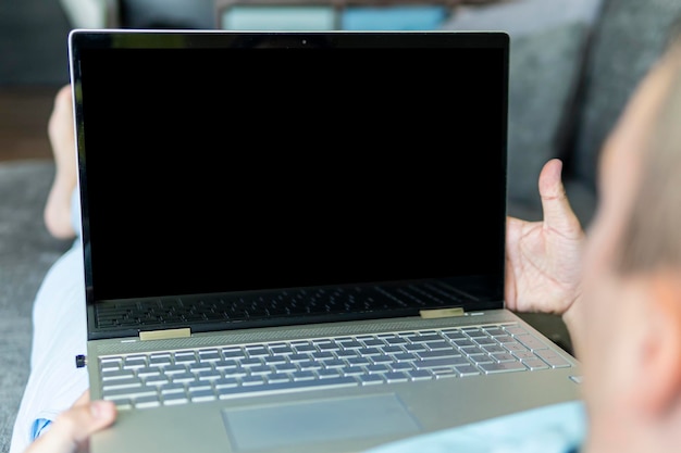 L'homme est allongé sur le canapé et regarde l'écran d'ordinateur portable noir vide Copier l'espace L'espace est vide pour le texte et la conception