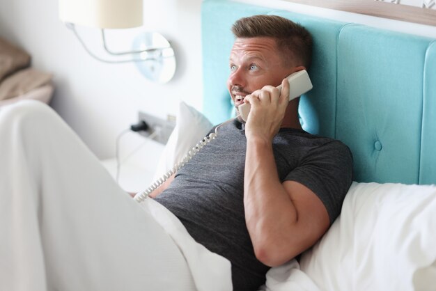 L'homme est allongé dans son lit dans la chambre d'hôtel et parle au téléphone.