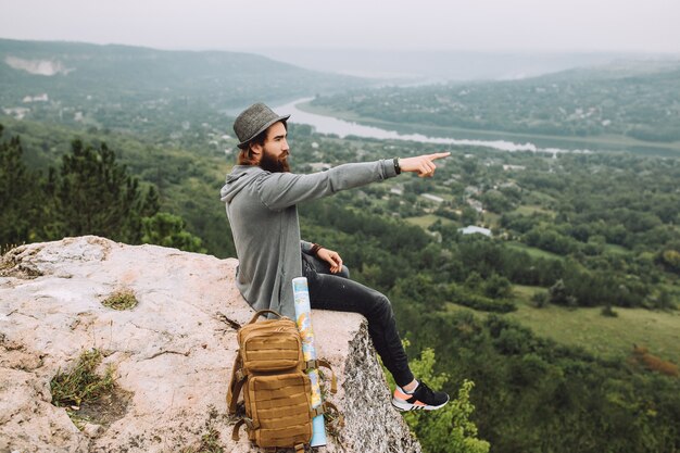 Un homme est assis au bord d'une falaise et se montre au loin.