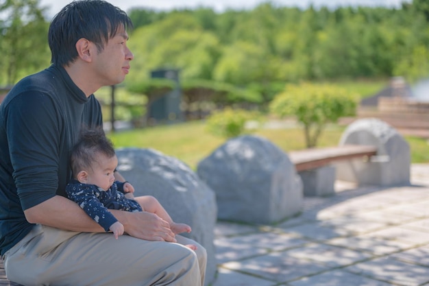 Un homme est assis sur un banc avec son bébé sur ses genoux.