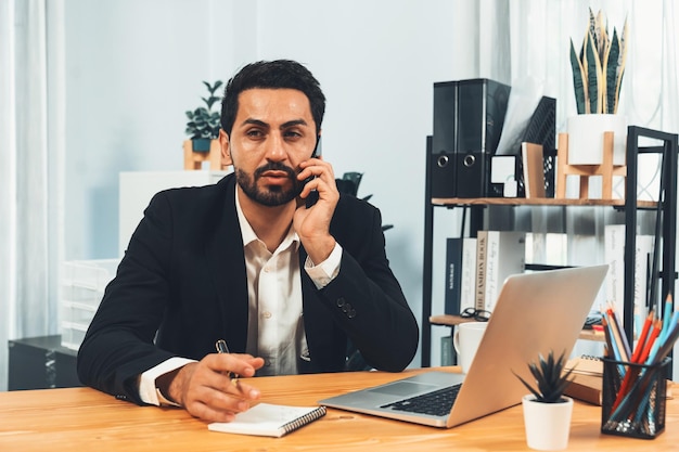 Un homme est assis à un bureau dans un bureau et parle au téléphone.