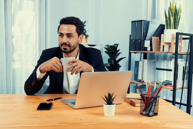 Un homme est assis à un bureau avec un ordinateur portable et un stylo sur la table.
