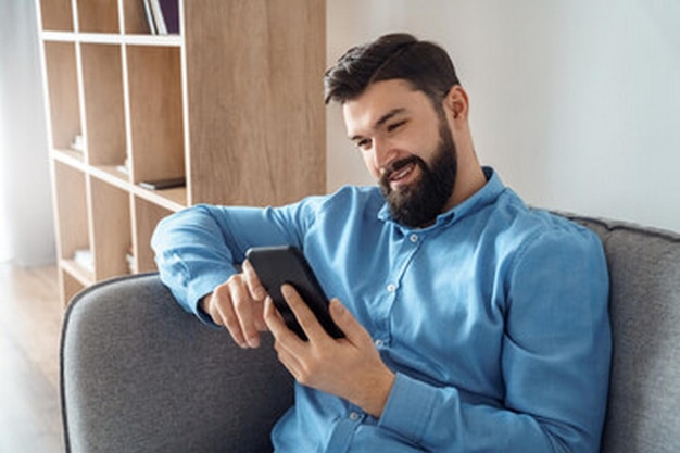un homme est assis sur un canapé et utilise une tablette